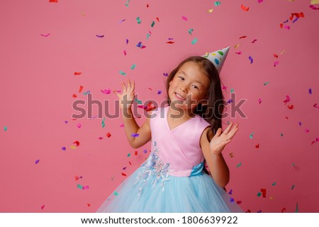 Asian girl celebrates birthday blows catches confetti on pink background