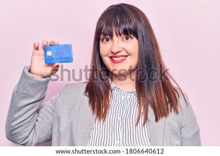 Young plus size woman holding credit card looking positive and happy standing and smiling with a confident smile showing teeth 