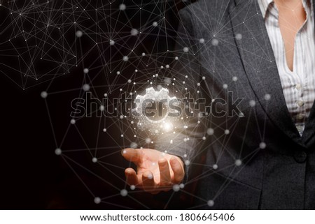 Businesswoman shows a hologram of gears on a dark background on the web.