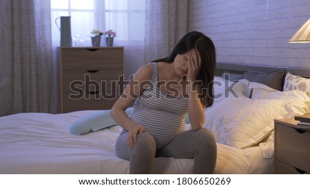 depressed sick pregnant female seated alone on bed late at night, pushing hair back and propping head. Royalty-Free Stock Photo #1806650269