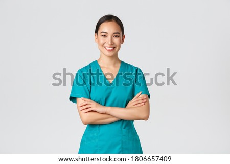 Covid-19, healthcare workers, pandemic concept. Confident smiling asian doctor, female nurse in scrubs standing determined, cross arms chest over white background. Doctor ready for shift in clinic Royalty-Free Stock Photo #1806657409