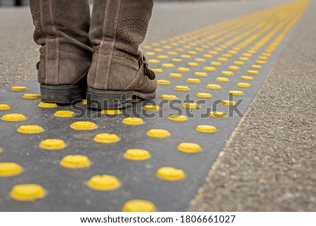 feet in shoes on special traffic signs for blind people in transport, accessible urban environment for visually impaired people