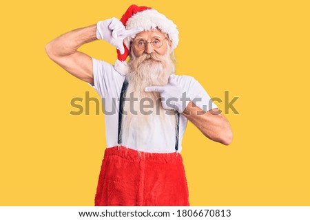 Old senior man with grey hair and long beard wearing santa claus costume with suspenders smiling making frame with hands and fingers with happy face. creativity and photography concept. 