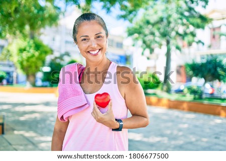 Middle age sportswoman asking for health care holding heart at the park Royalty-Free Stock Photo #1806677500