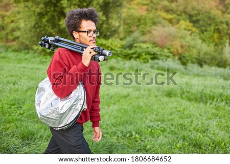 Young nature photographer with tripod on the shoulder on motive search in nature