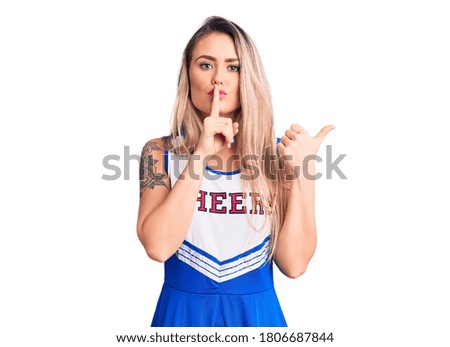 Young beautiful blonde woman wearing cheerleader uniform asking to be quiet with finger on lips pointing with hand to the side. silence and secret concept. 