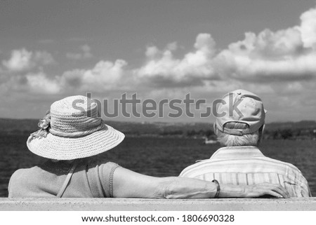 Elderly couple sitting on a bench by the lake. Black and white photo.