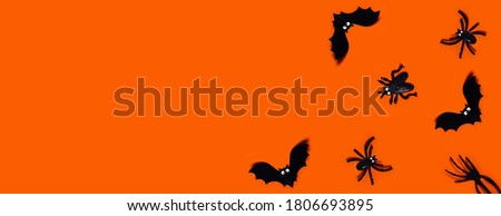 Halloween web banner - orange background with spiders, bats, hand. Flat lay with a place for your text. Plastic toys.
