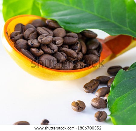 Coffee beans in a wooden spoon on a white background. Some of the grains spilled onto the table.