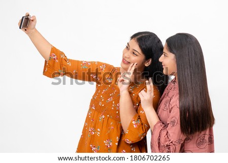Two young teenager Indian girls take photos on their smart phone