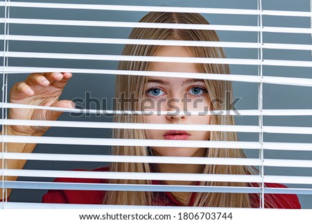 Curious girl looks through the blinds