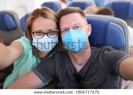 Husband and wife take selfie on plane wearing medical masks. Travel during epidemic coronavirus infection concept