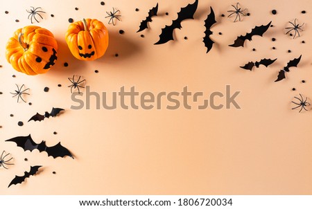 Halloween decorations made from pumpkin, paper bats and black spider on pastel orange background. Flat lay, top view with copy space for text.