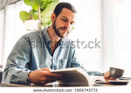 Handsome hipster man relaxing read the paper book work study and looking at page magazine while sitting on chair in cafe and restaurant