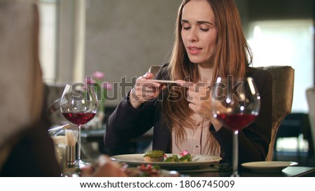 Businesswoman taking food photo on smartphone at restaurant. Smiling woman photographing dish on mobile phone in cafe.