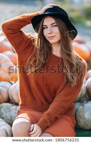 Portrait of happy woman sitting on farmers market with orange pumpkin in brown sweater and hat. Cozy autumn vibes Halloween, Thanksgiving day.