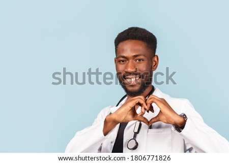 African American male doctor with stethoscope in white coat shows heart sign with hands on blue background. medicine, profession and healthcare concept.