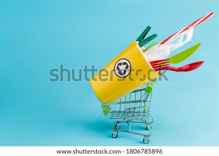 yellow recycling bin with plastic in small shopping cart on blue background