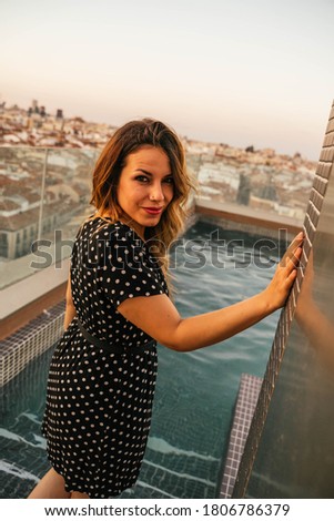 Young blonde woman in dress smiling in the pool of a rooftop in the city of Madrid during sunset