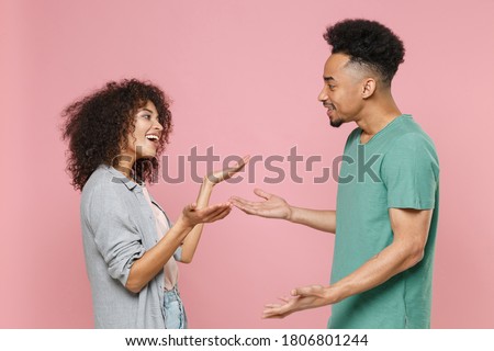 Side view of cheerful excited young african american couple two friends man woman in gray green casual clothes spreading hands speaking talking isolated on pastel pink color background studio portrait Royalty-Free Stock Photo #1806801244