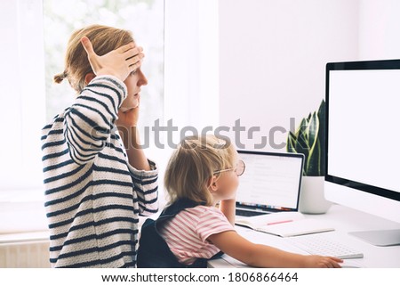 Modern mom balances between work and child home schooling on sick leave or quarantine. Mother works from home with kid. Woman responding on phone calls, working on computer with a toddler on her lap.