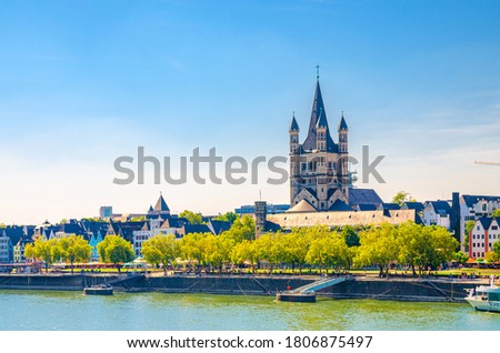 Cologne cityscape of historical city centre with Great Saint Martin Roman Catholic Church tower buildings and trees on embankment of Rhine river, blue sky background, North Rhine-Westphalia, Germany