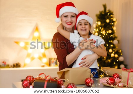 Cheerful pretty mother and her adorable little daughter enjoying beauty of handmade Christmas decoration while sitting at desk, interior of cozy living room on background