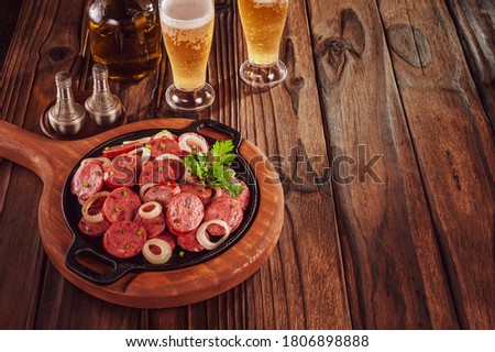 Sliced smoked fried calabrese sausage with onion and beer - Brazilian appetizer with space copy