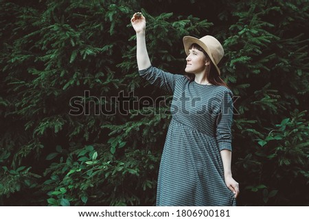 Beautiful red-haired young woman in a straw hat and dress on a background of green forest and trees. Place for text or advertising