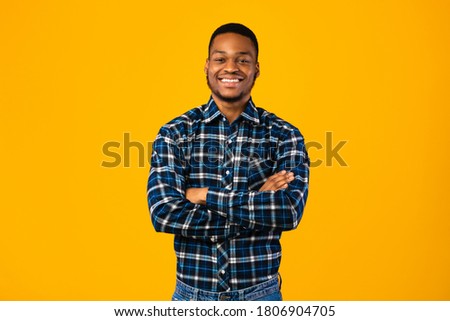 Black Man Posing Crossing Hands Smiling To Camera Standing In Studio Over Yellow Background. Millennial's Portrait Royalty-Free Stock Photo #1806904705