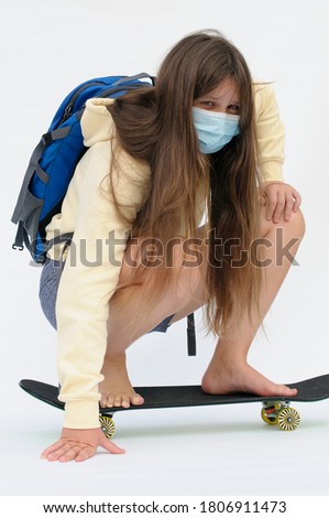 The vertical photo of a long-hair, teenaged girl with a backpack and the disposable mask on the face on the skateboard over the white background