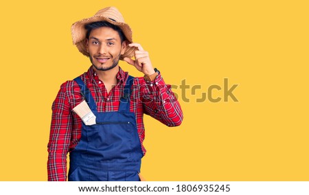 Handsome latin american young man weaing handyman uniform smiling and confident gesturing with hand doing small size sign with fingers looking and the camera. measure concept. 