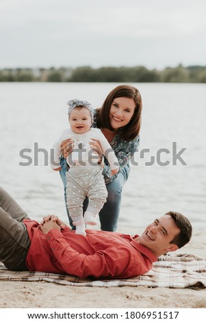 Happy young family sitting near the water. Mom, dad and their little baby daughter sitting together. Happy family outdoors. Smiling people.