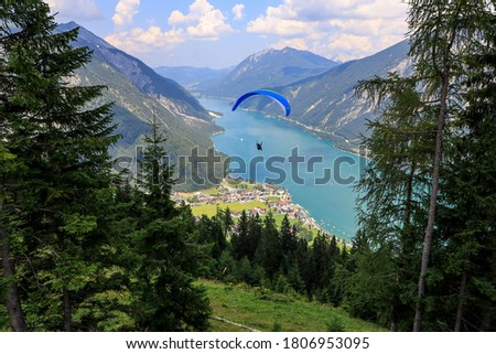 A paraglider above Achen lake, a picturesque alpine  lake with shimmering turquoise waters, offering swimming, sailing, boating and hiking. A view from the cable car station above Pertisau.  Royalty-Free Stock Photo #1806953095