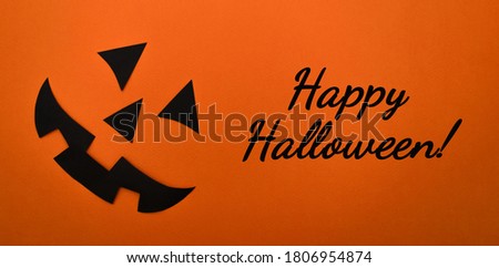 Black eyes,nose and mouth of black paper on an orange background.The inscription HAPPY HALLOWEEN! on an orange background.Halloween concept.