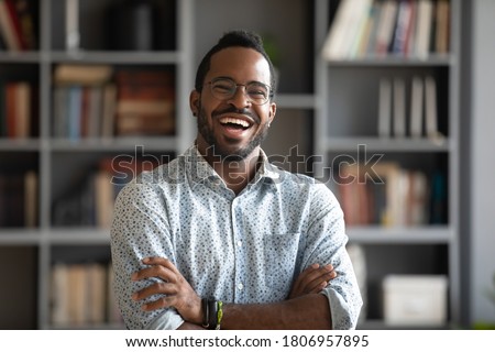 Head shot portrait laughing excited African American man wearing glasses standing with arms crossed in modern cabinet, positive young male confident businessman in eyewear looking at camera Royalty-Free Stock Photo #1806957895