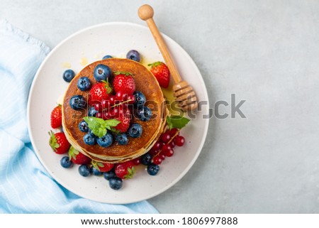 Top view of pancakes with honey, strawberries, red currant and blueberries. Royalty-Free Stock Photo #1806997888