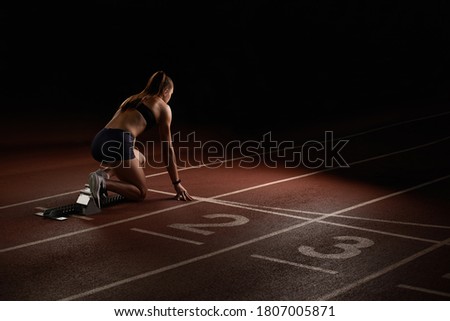 Woman athlete sprinter preparing for start on the sport arena.