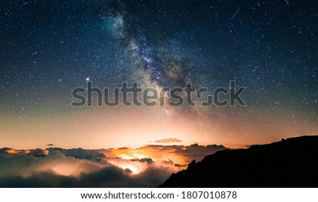 Starry sky above a sea of clouds with the lights of the cities and villages below producing orange light pollution. Night photography of long exposure landscapes with the Milky Way.