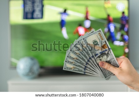 The winner at football betting holds a dollar money prize in hand near the TV Royalty-Free Stock Photo #1807040080