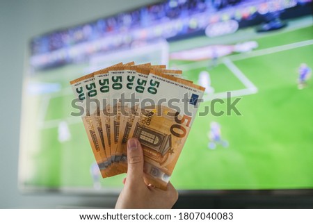 The winner at football betting holds a dollar money prize in hand near the TV Royalty-Free Stock Photo #1807040083