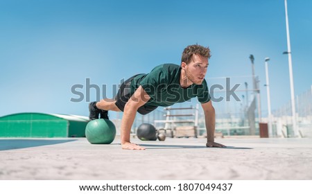Fit exercises man strength training core doing balance push-ups workout at outdoor gym balancing on stability medicine ball with legs. Bodyweight pushups exercises. Push-up variation. Royalty-Free Stock Photo #1807049437