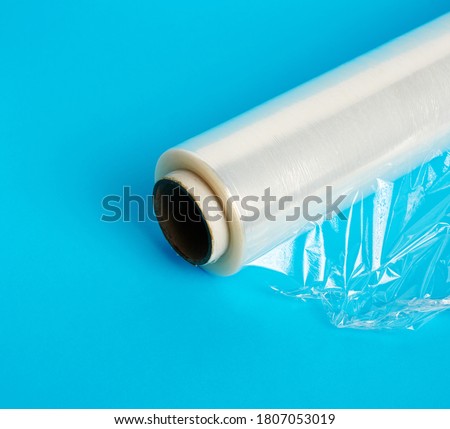 big roll of wound white transparent film for wrapping food, blue background, close up