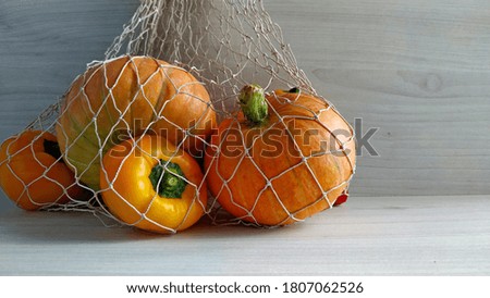 harvest time. Pumpkins and yellow and red peppers in a string bag on a light wood background.