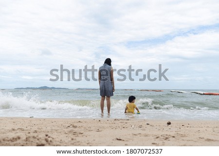 Mother and 3 years old asian kid playing on the beach. Background for family vacation and recreation.