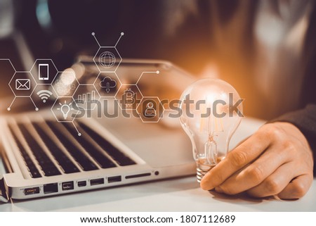 Hand holding Light bulb in office,with icons holographic,Business woman planning work with laptop working on white desk.in office blurred background.