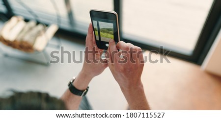 Close up of man hands taking picture of the beautiful view outside the window with mobile phone. Businessman using smartphone in his modern house to photograph the mountains through the window