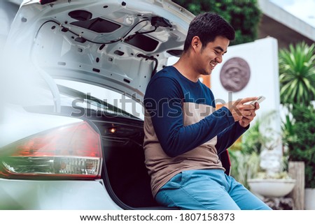 Asian thai casual traveler man using smartphone at trunk car.