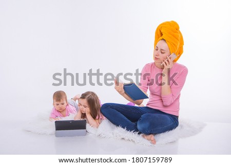 woman with book in her hands is talking on phone. Children watch cartoon on their tablet. mom washed her hair. towel on head. Hobbies and recreation with gadgets.