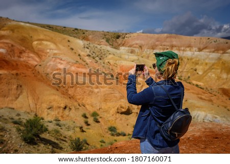 Female tourist takes pictures of amazing natural phenomenon on her smartphone. Colorful mountains in the Altai. Travel in Russia. Unknown planet.